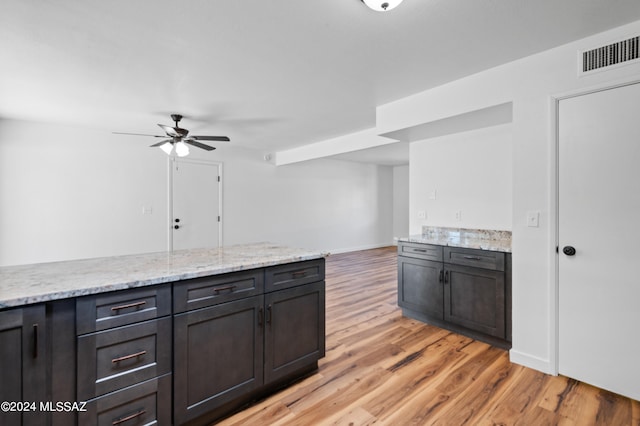 kitchen with dark brown cabinets, light hardwood / wood-style floors, ceiling fan, and light stone counters