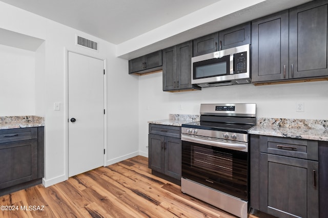 kitchen with light stone countertops, appliances with stainless steel finishes, and light hardwood / wood-style flooring