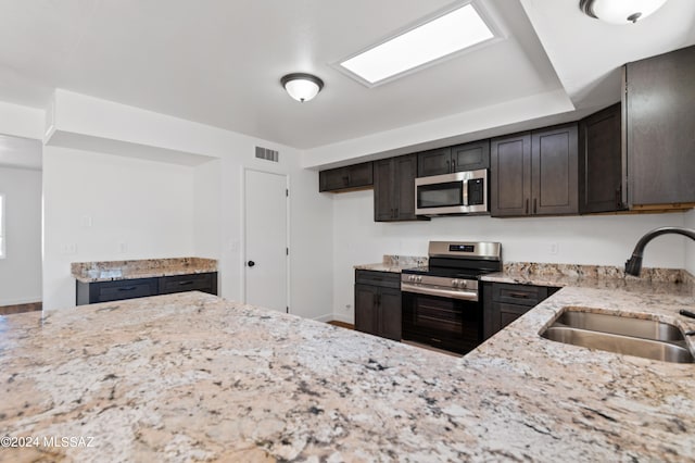 kitchen featuring dark brown cabinetry, appliances with stainless steel finishes, light stone counters, and sink