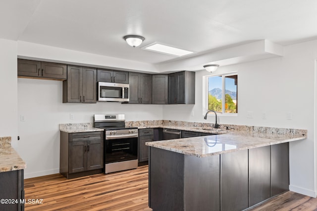 kitchen featuring light stone counters, sink, kitchen peninsula, appliances with stainless steel finishes, and light wood-type flooring