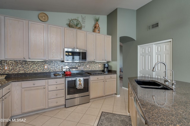 kitchen with high vaulted ceiling, sink, dark stone countertops, appliances with stainless steel finishes, and light tile patterned flooring