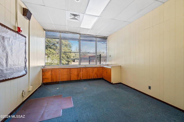 interior space with a paneled ceiling, wood walls, and dark carpet