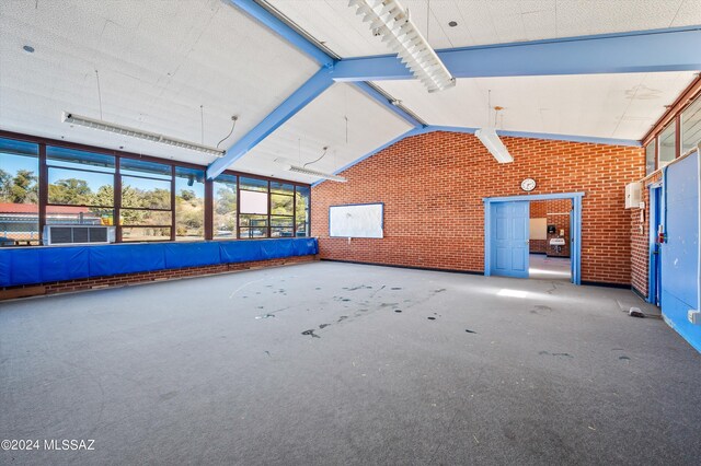 interior space featuring brick wall, lofted ceiling, carpet, and a wall unit AC