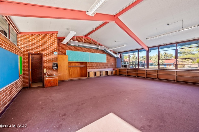 interior space featuring lofted ceiling with beams, brick wall, and carpet floors