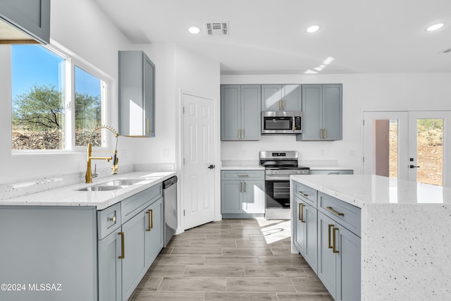 kitchen featuring gray cabinetry, sink, light stone counters, and appliances with stainless steel finishes