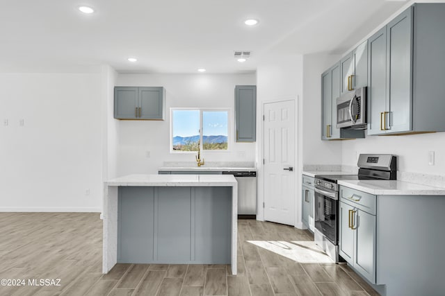 kitchen with gray cabinetry, stainless steel appliances, light wood-type flooring, light stone countertops, and a center island