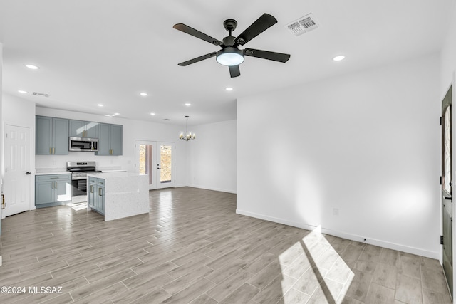 unfurnished living room featuring ceiling fan with notable chandelier and light hardwood / wood-style flooring