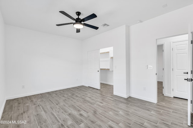 unfurnished bedroom featuring a closet, a walk in closet, ceiling fan, and light hardwood / wood-style flooring