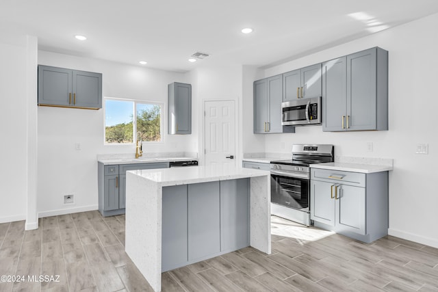 kitchen featuring stainless steel appliances, light stone counters, a center island, gray cabinets, and light wood-type flooring