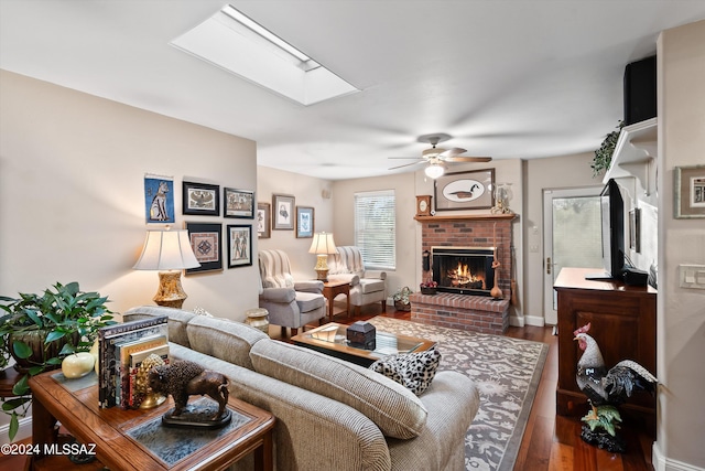 living room with a brick fireplace, ceiling fan, a skylight, and hardwood / wood-style floors