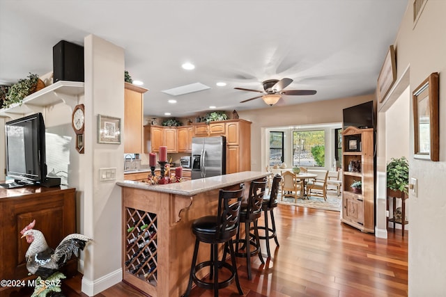 kitchen featuring kitchen peninsula, wood-type flooring, a kitchen bar, ceiling fan, and stainless steel fridge with ice dispenser