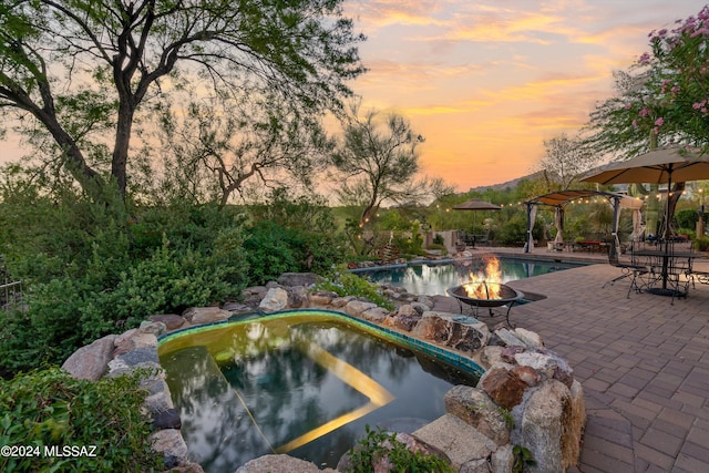 pool at dusk featuring a fire pit, a pergola, a patio, and a hot tub