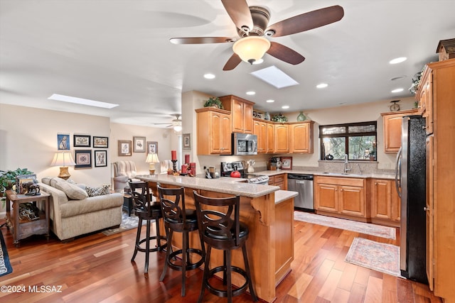 kitchen with wood-type flooring, sink, a breakfast bar area, stainless steel appliances, and a skylight