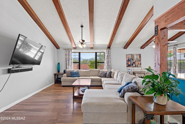 living area with a ceiling fan, wood finished floors, a textured ceiling, lofted ceiling with beams, and baseboards