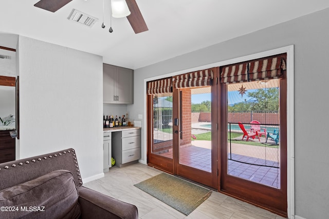 doorway to outside with marble finish floor, ceiling fan, a dry bar, baseboards, and visible vents