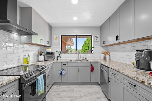 kitchen featuring appliances with stainless steel finishes, wall chimney exhaust hood, sink, and gray cabinetry