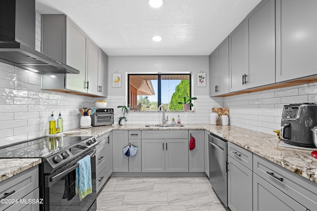 kitchen featuring wall chimney range hood, stainless steel dishwasher, a sink, black electric range, and gray cabinets