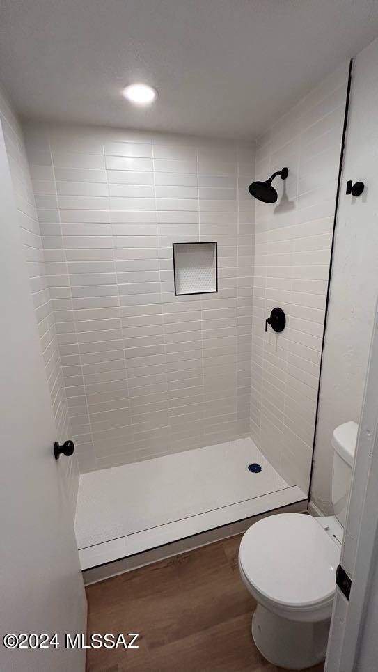 bathroom featuring a tile shower, hardwood / wood-style floors, and toilet