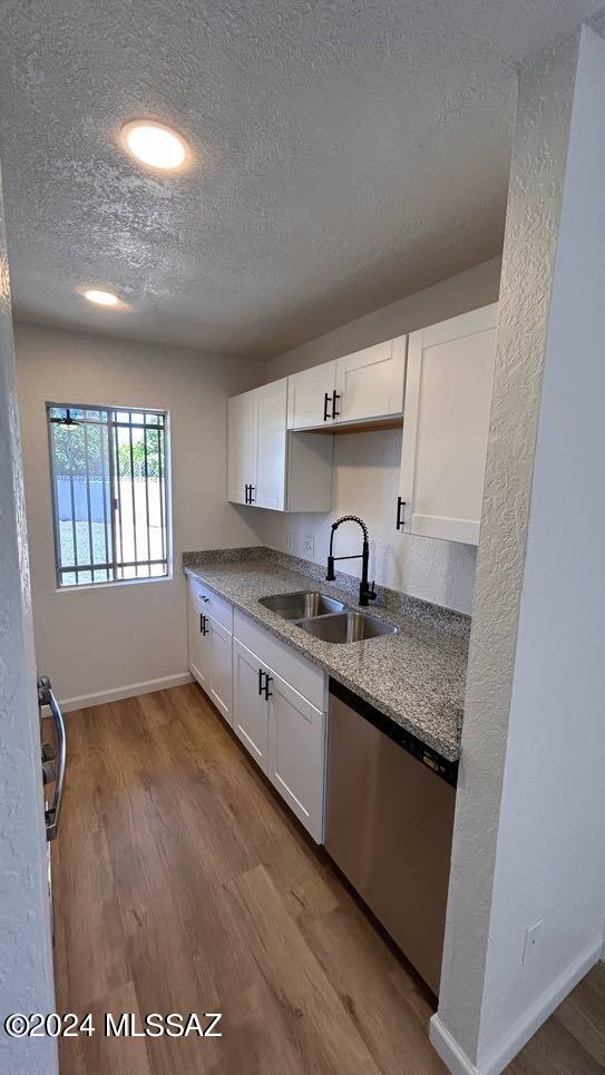 kitchen with sink, stainless steel dishwasher, a textured ceiling, white cabinetry, and light wood-type flooring