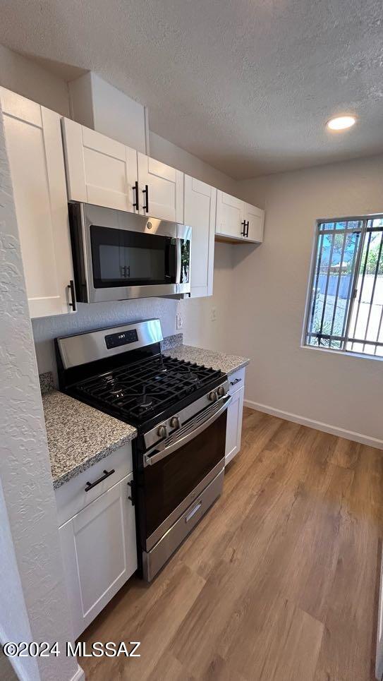 kitchen featuring light hardwood / wood-style flooring, stainless steel appliances, white cabinetry, and light stone countertops