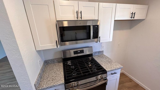 kitchen with stainless steel appliances, white cabinets, light stone counters, and dark wood-type flooring