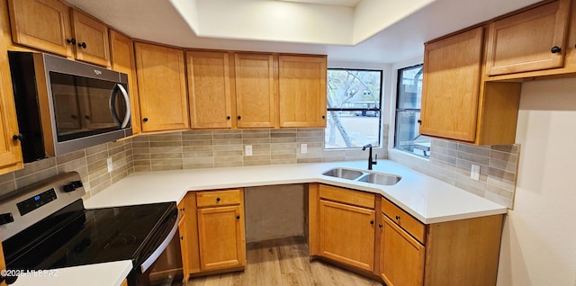 kitchen with brown cabinetry, light wood finished floors, a sink, stainless steel appliances, and backsplash