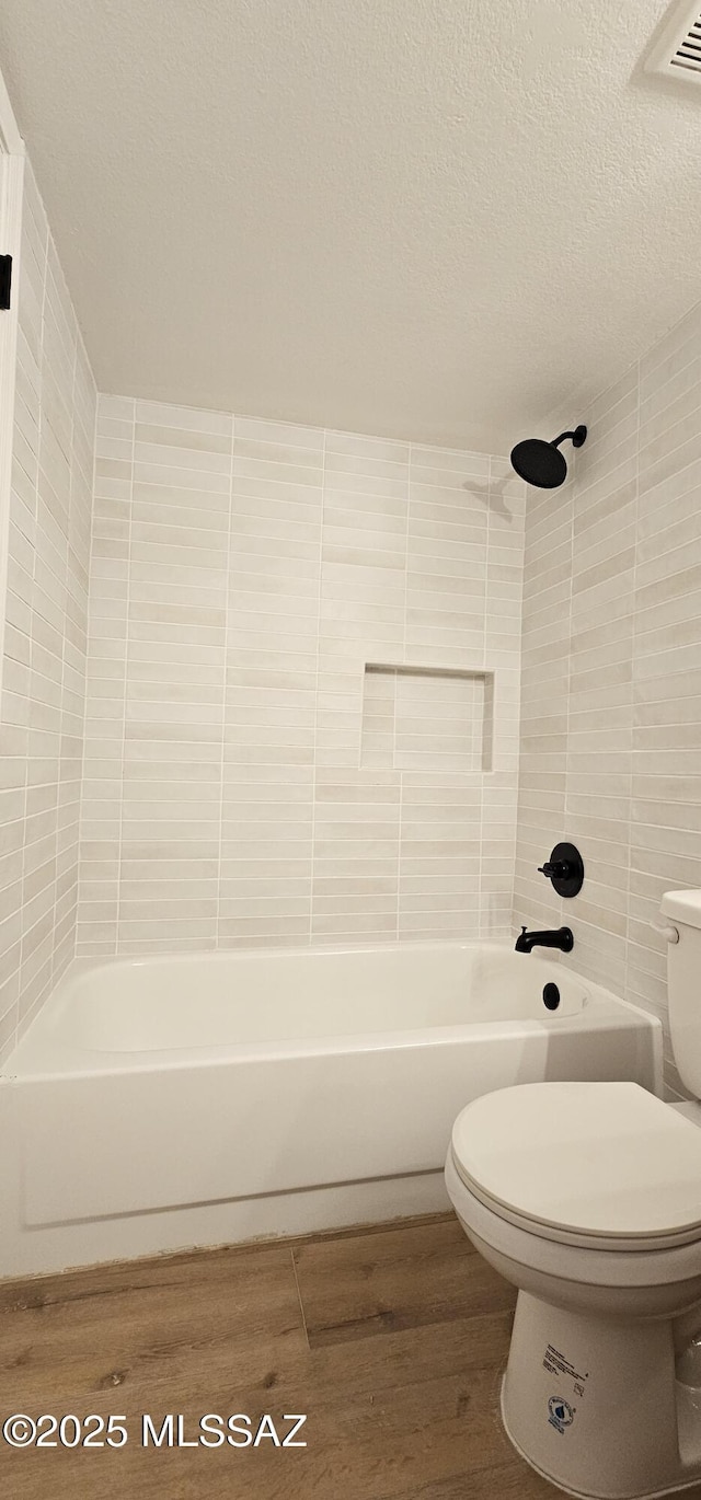 bathroom with wood finished floors, bathtub / shower combination, a textured ceiling, tile walls, and toilet