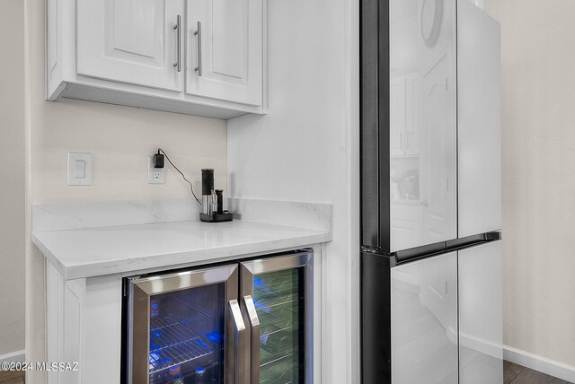 bar with stainless steel fridge, wood-type flooring, wine cooler, and white cabinets