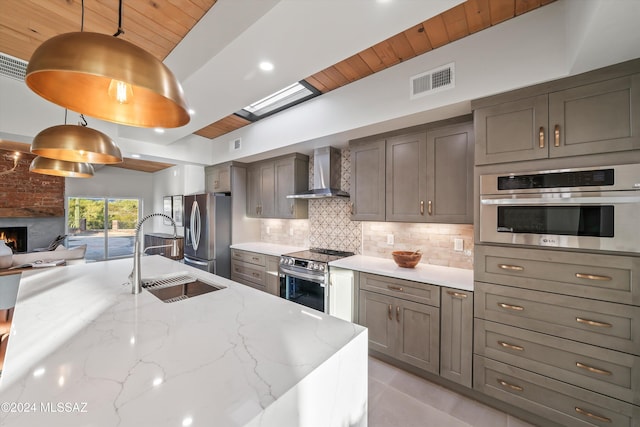 kitchen featuring sink, hanging light fixtures, stainless steel appliances, wall chimney range hood, and light stone counters