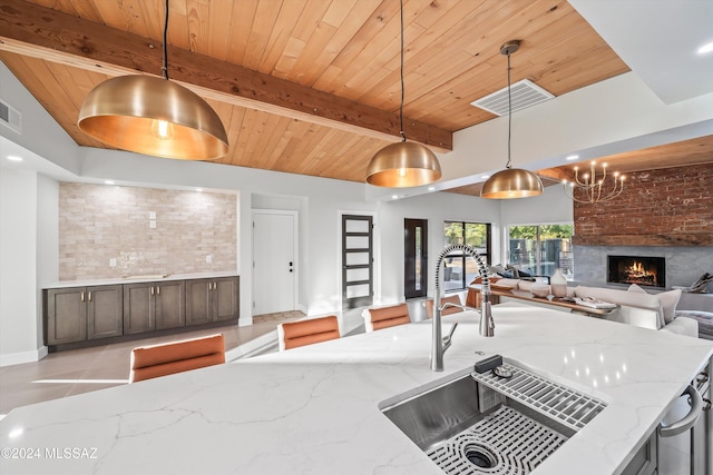 kitchen with light stone countertops, beam ceiling, decorative light fixtures, and sink