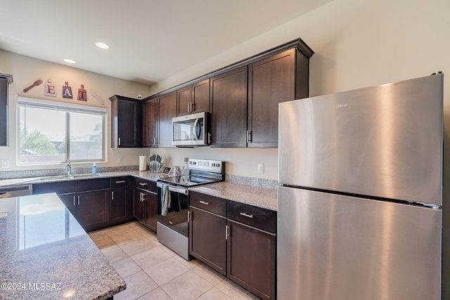 kitchen featuring light tile patterned flooring, appliances with stainless steel finishes, sink, dark brown cabinetry, and light stone counters