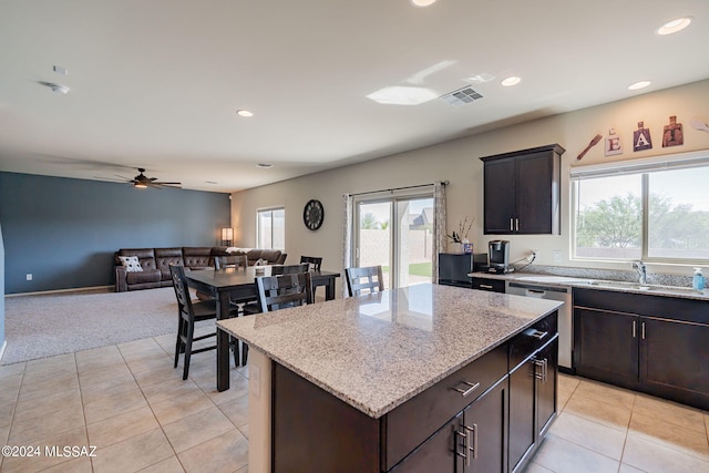 kitchen with light colored carpet, dark brown cabinets, dishwasher, a kitchen island, and ceiling fan