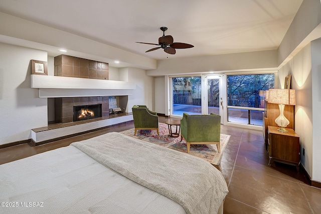 bedroom with a tile fireplace, access to outside, and ceiling fan