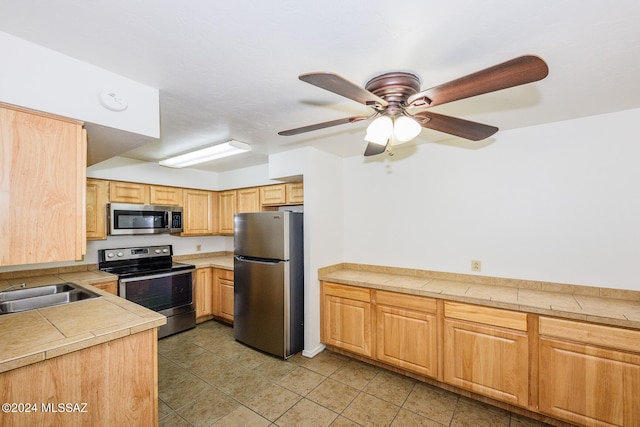 kitchen with light tile patterned floors, stainless steel appliances, ceiling fan, tile counters, and sink