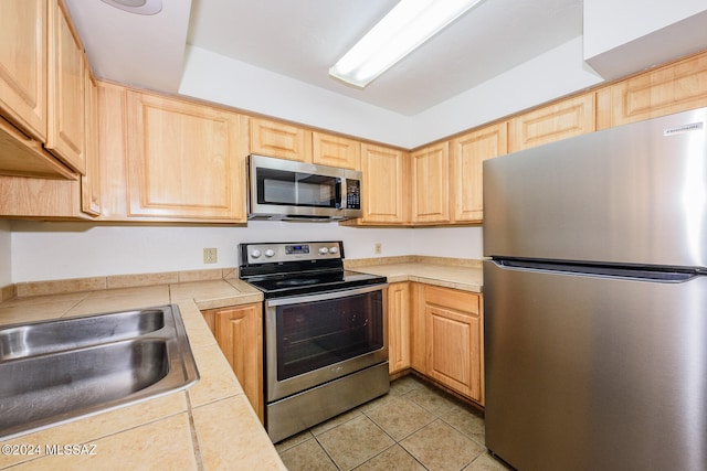 kitchen with stainless steel appliances, light brown cabinets, light tile patterned floors, and sink