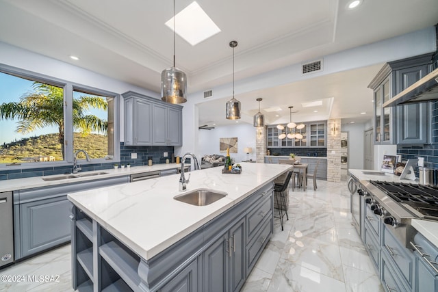 kitchen with gray cabinets, a kitchen island with sink, sink, and decorative backsplash