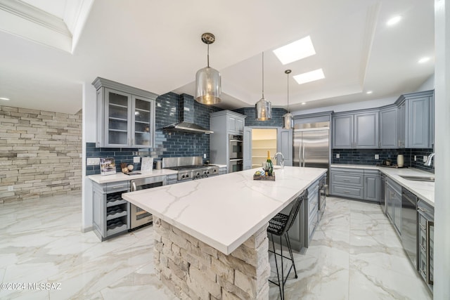 kitchen featuring an island with sink, hanging light fixtures, tasteful backsplash, and wall chimney range hood