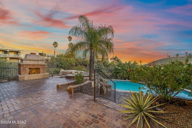 pool at dusk with an outdoor stone fireplace and a patio area