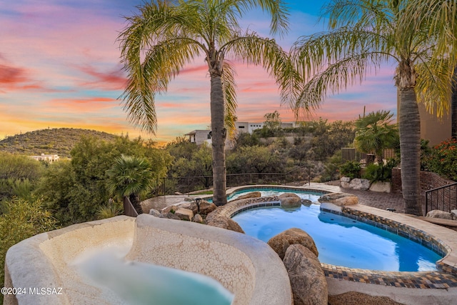 pool at dusk featuring an in ground hot tub