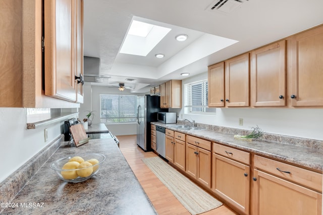 kitchen featuring ceiling fan, light brown cabinets, a skylight, light hardwood / wood-style flooring, and appliances with stainless steel finishes