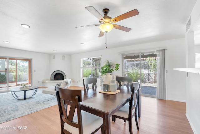 dining room featuring ceiling fan, light hardwood / wood-style floors, a large fireplace, and a healthy amount of sunlight