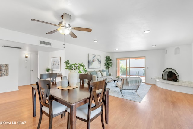 dining room with a large fireplace, light hardwood / wood-style floors, and ceiling fan