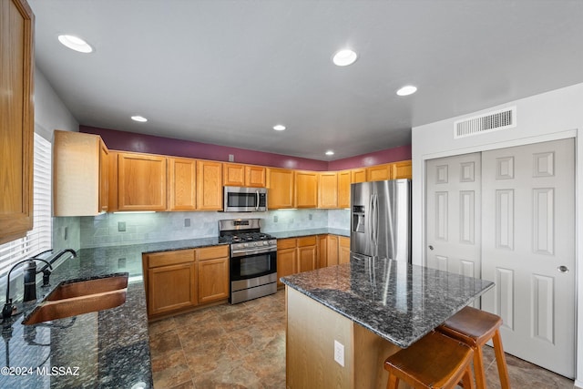 kitchen with appliances with stainless steel finishes, a breakfast bar area, dark stone countertops, and sink