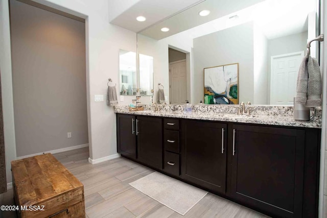 bathroom featuring wood finished floors, a sink, double vanity, baseboards, and recessed lighting