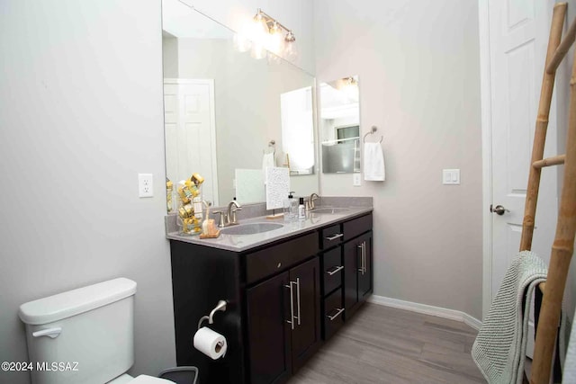 bathroom with toilet, wood finished floors, a sink, and double vanity