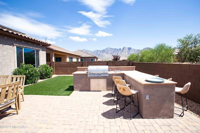 view of patio / terrace featuring exterior kitchen, a fenced backyard, a mountain view, outdoor dry bar, and grilling area