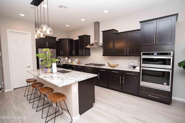 kitchen with a sink, visible vents, wall chimney range hood, light stone countertops, and appliances with stainless steel finishes