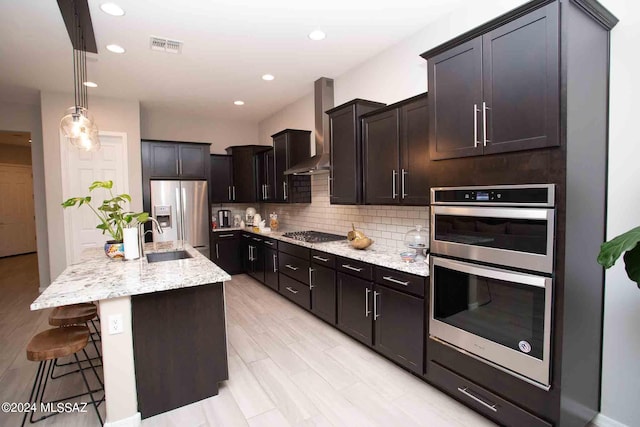 kitchen with an island with sink, backsplash, wall chimney exhaust hood, a breakfast bar area, and stainless steel appliances