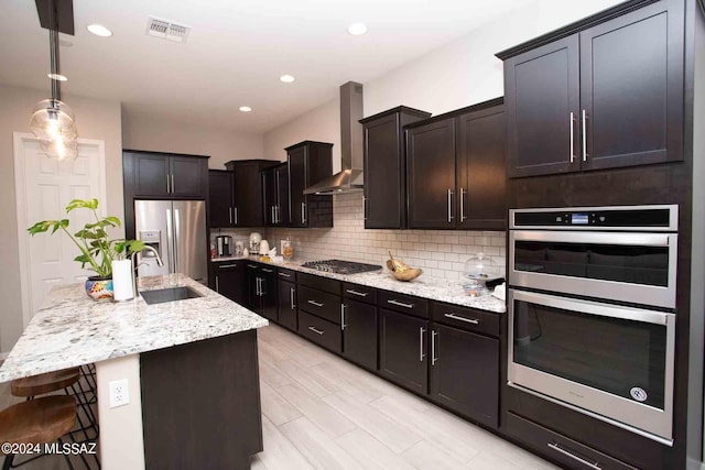 kitchen with light stone counters, tasteful backsplash, a sink, wall chimney exhaust hood, and appliances with stainless steel finishes