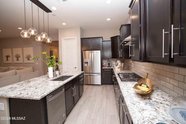 kitchen with sink, an island with sink, decorative backsplash, stainless steel appliances, and dark brown cabinetry